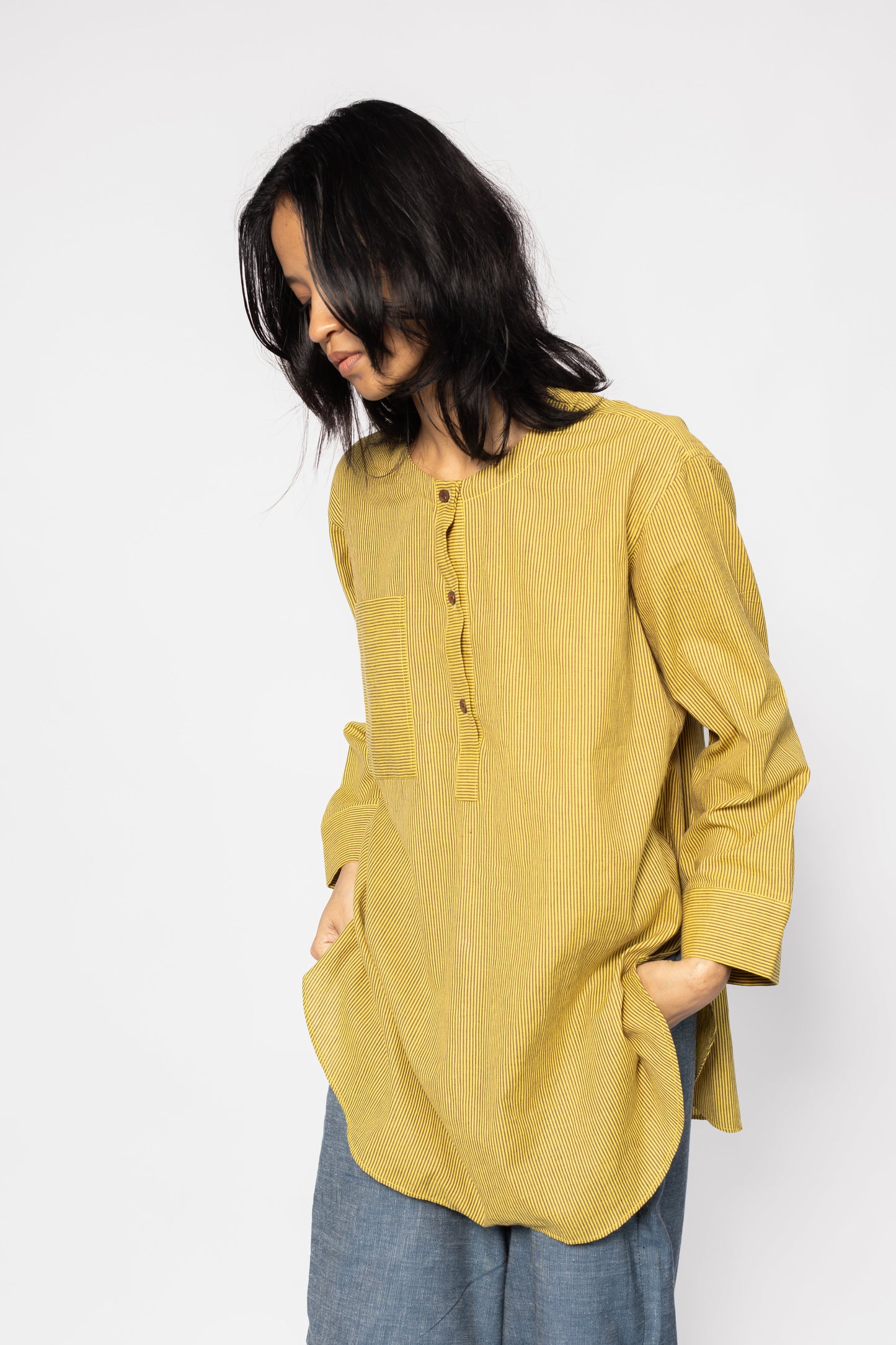 Plains Design - Harvest oversized shirt. Mustard yellow oversized shirt tunic with brown stripes featuring a rounded hem and side slits, wooden buttons, and front chest pocket. The tunic is made from handwoven cotton and has a relaxed fit with a patch pocket on one side.