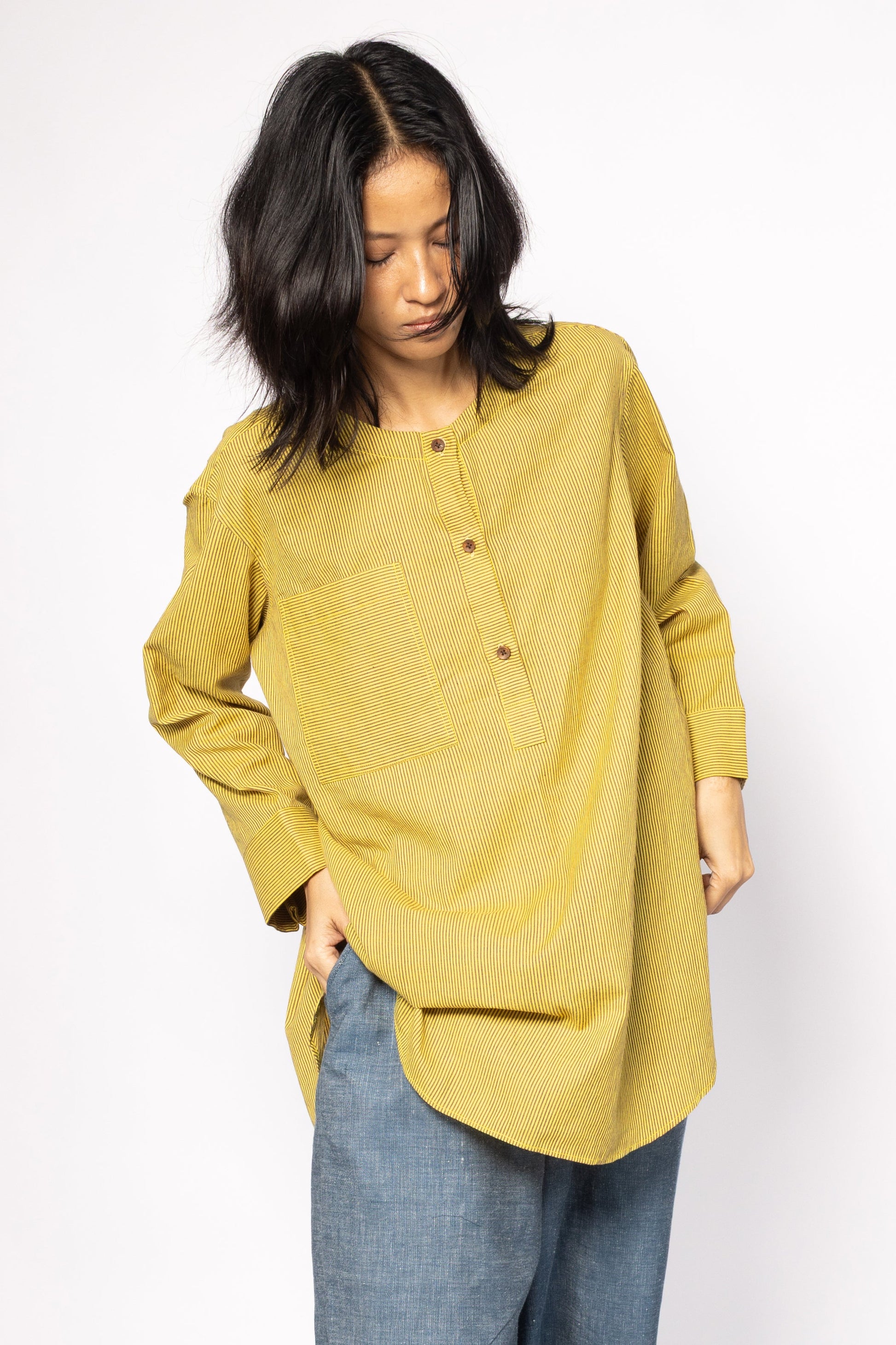 Plains Design - Harvest oversized shirt. Mustard yellow oversized shirt tunic with brown stripes featuring a rounded hem and side slits, wooden buttons, and front chest pocket. The tunic is made from handwoven cotton and has a relaxed fit. Paired with denim pants.