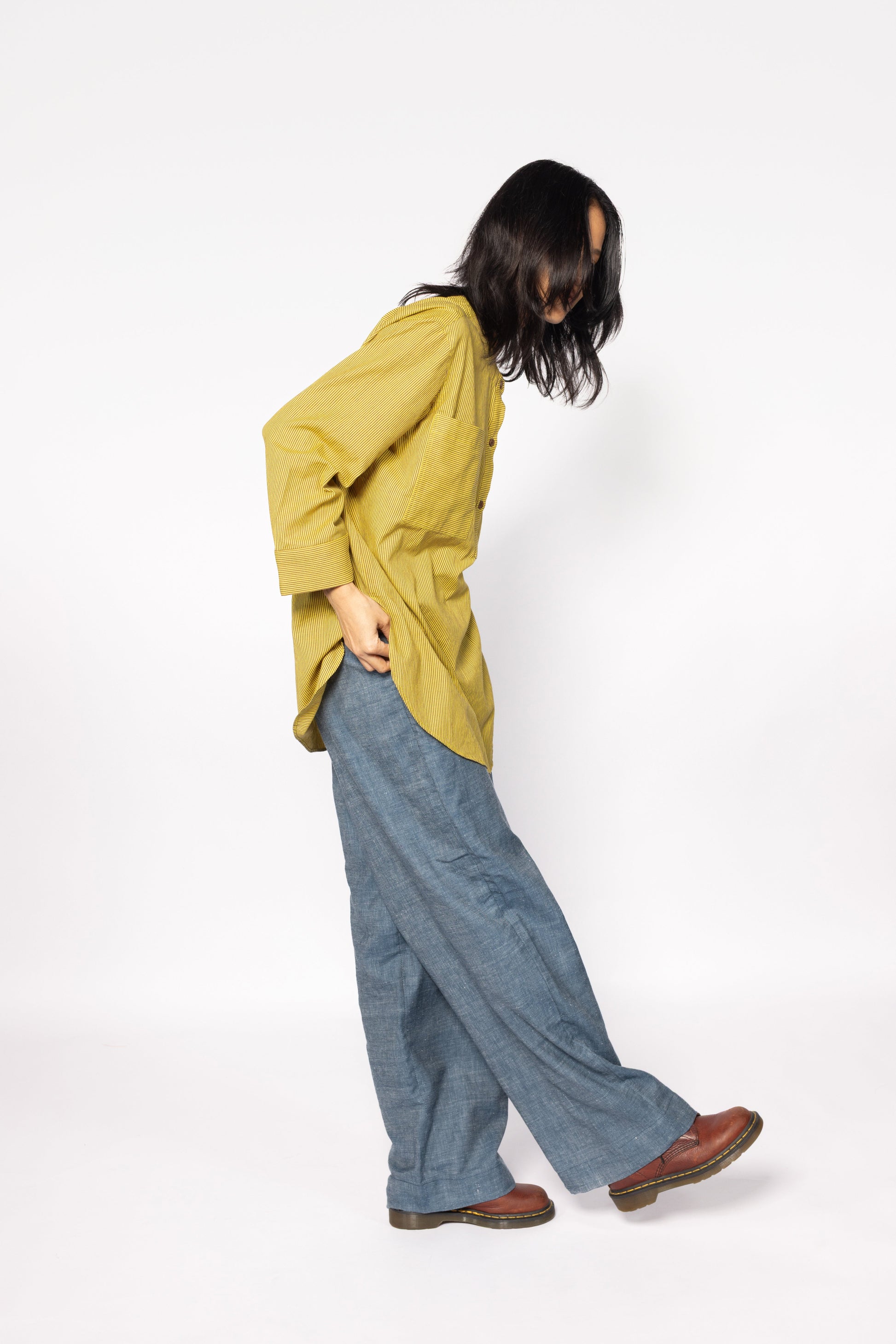 Plains Design - Harvest oversized shirt. Mustard yellow oversized shirt with brown stripes, wooden buttons, and front chest pocket, paired with blue jeans and brown shoes.