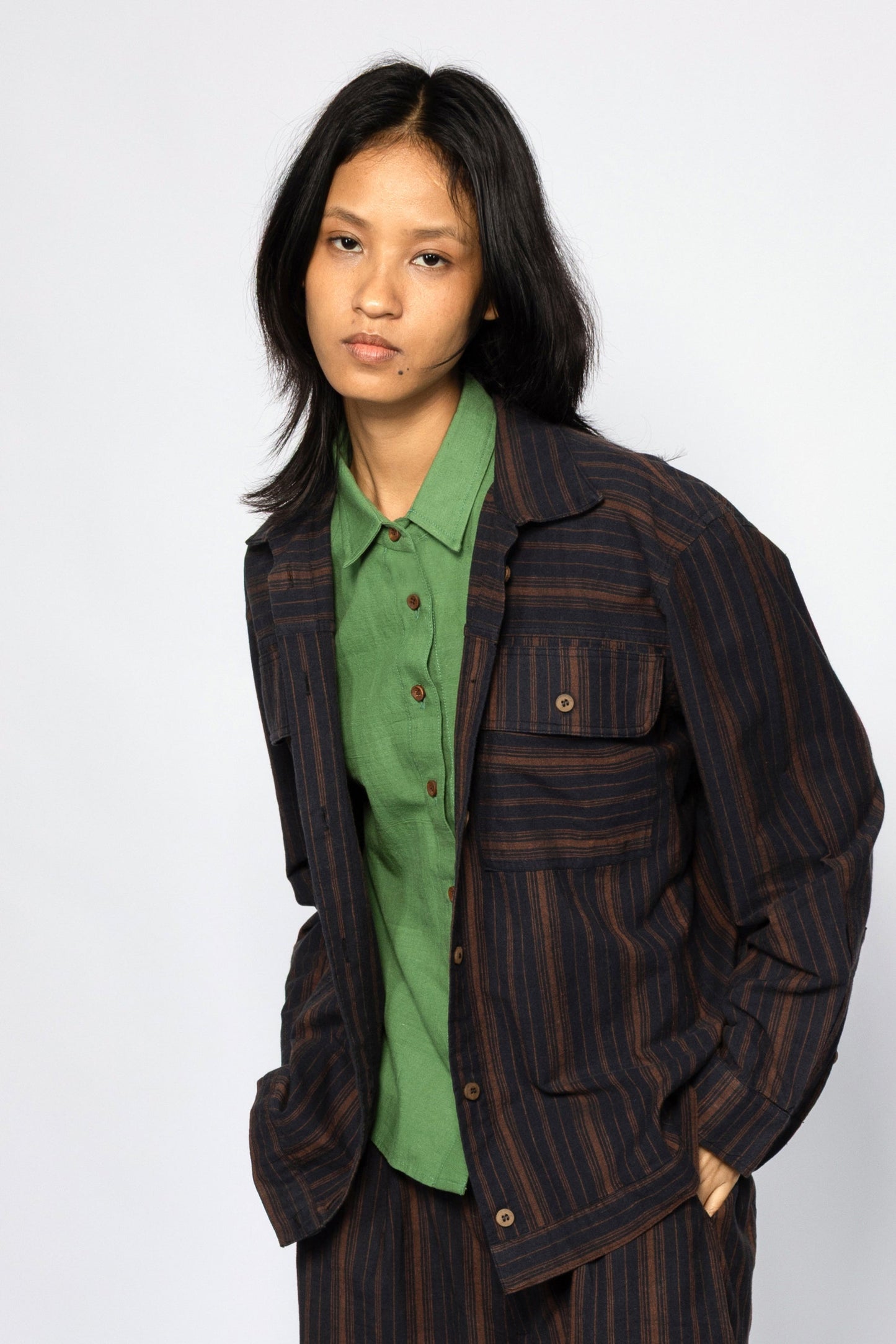 Plains Design - Brick Shirt. Oversized striped shirt in black and brick colours with long sleeves and square flap pockets on the chest. The shirt has contrasting stripes in a different direction on the pockets and sleeve hem. Paired with pants of the same handwoven cotton fabric.