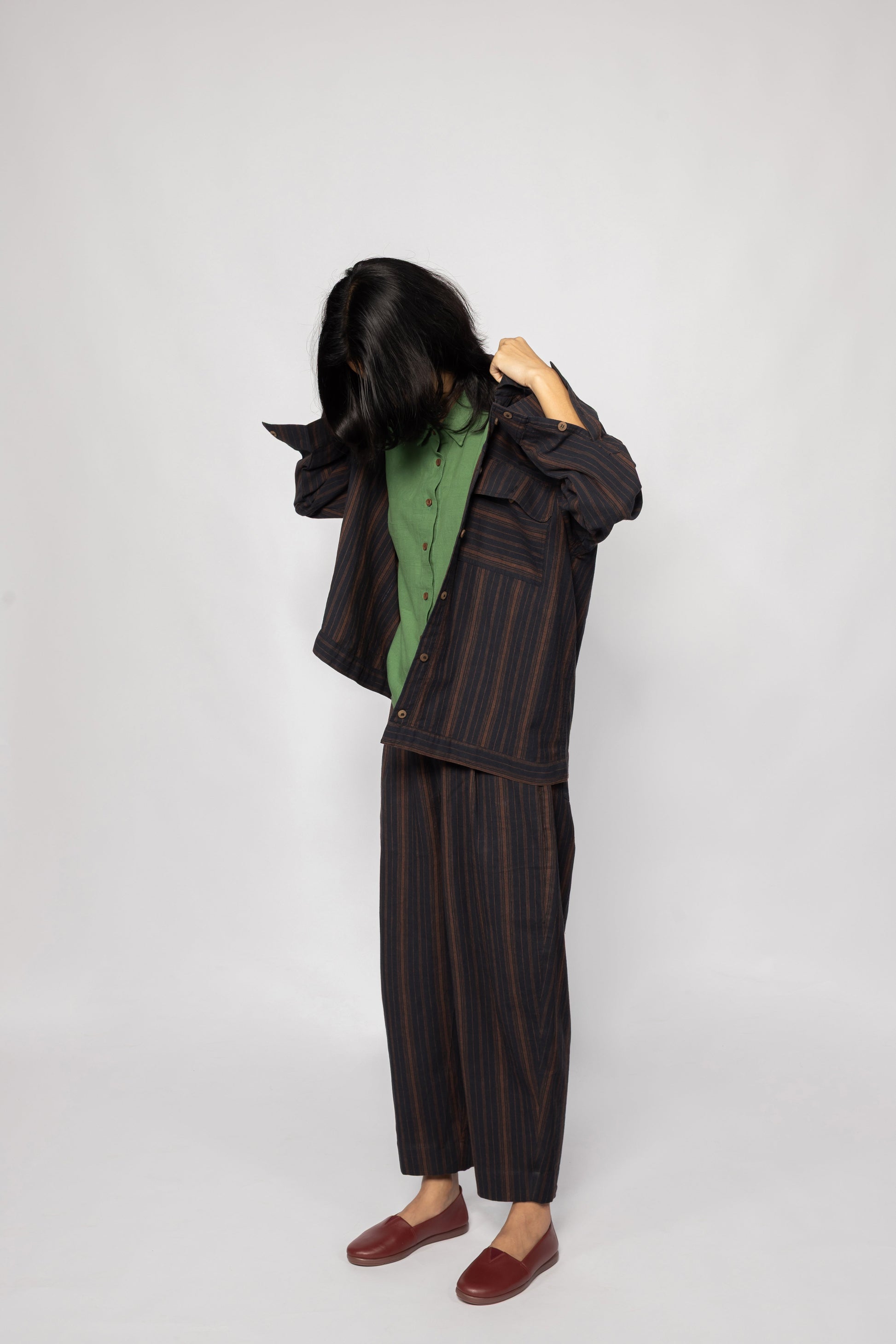 Plains Design - Brick Shirt. Oversized striped shirt in black and brick colours with long sleeves and square flap pockets on the chest. The shirt has contrasting stripes in a different direction on the pockets and sleeve hem. Paired with pants of the same handwoven cotton fabric.