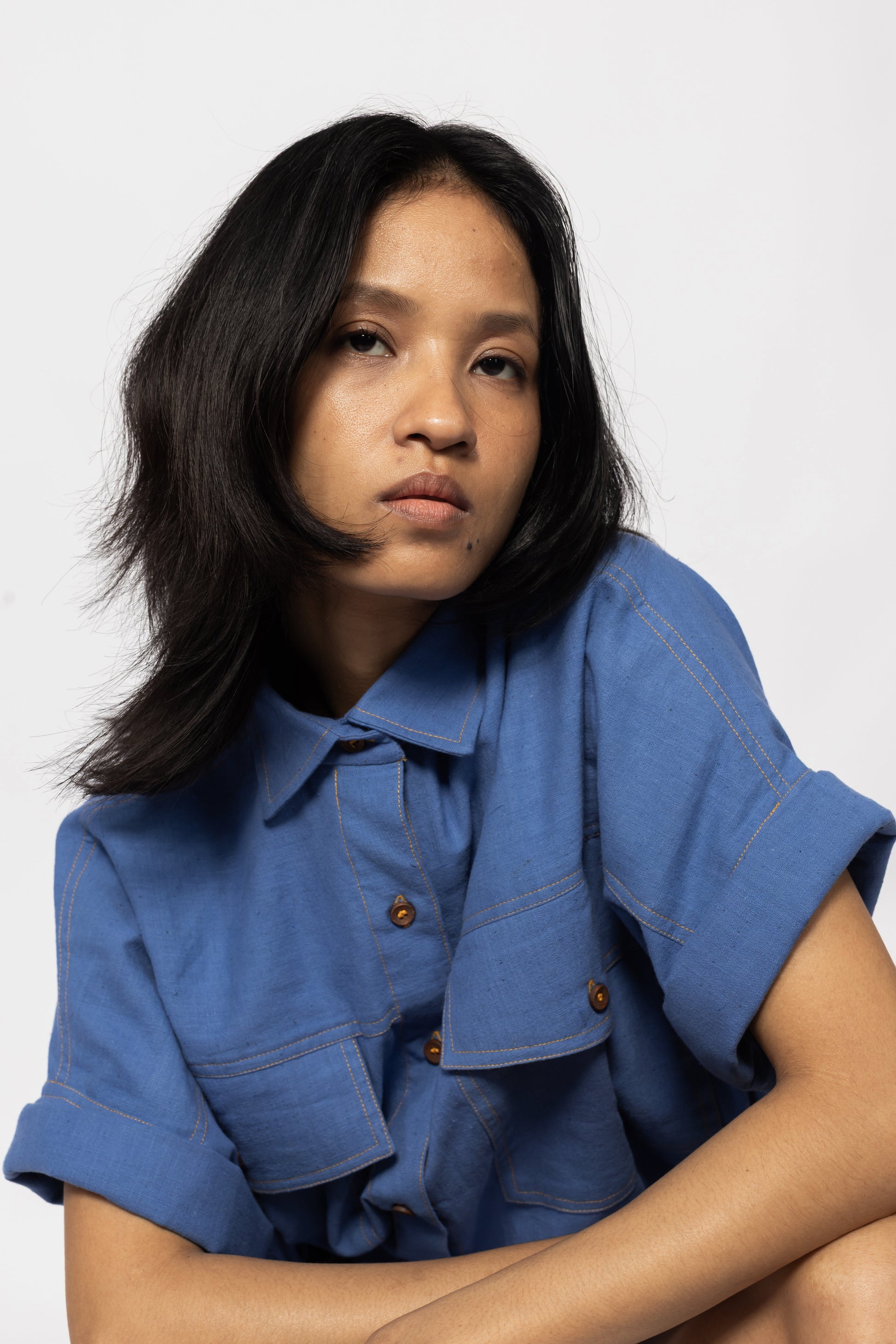 Plains Design - Trucker shirt. Close up of a person wearing a blue cotton shirt with orange stitching and wooden buttons. Sustainable handmade cotton.