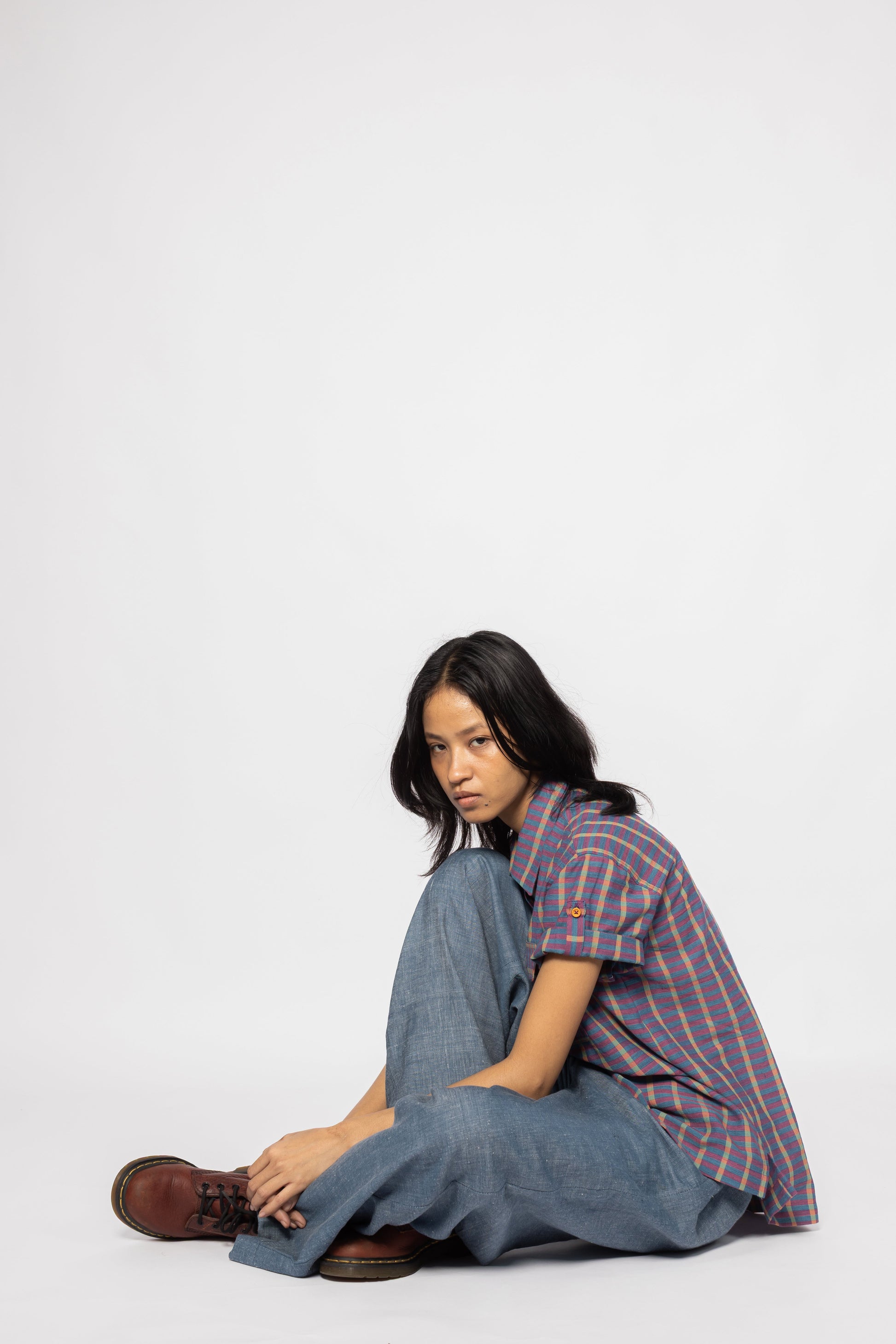 Plains Design Billie Denim Pants – model sitting on floor wearing handwoven cotton denim wide-leg pants and striped shirt, relaxed everyday style