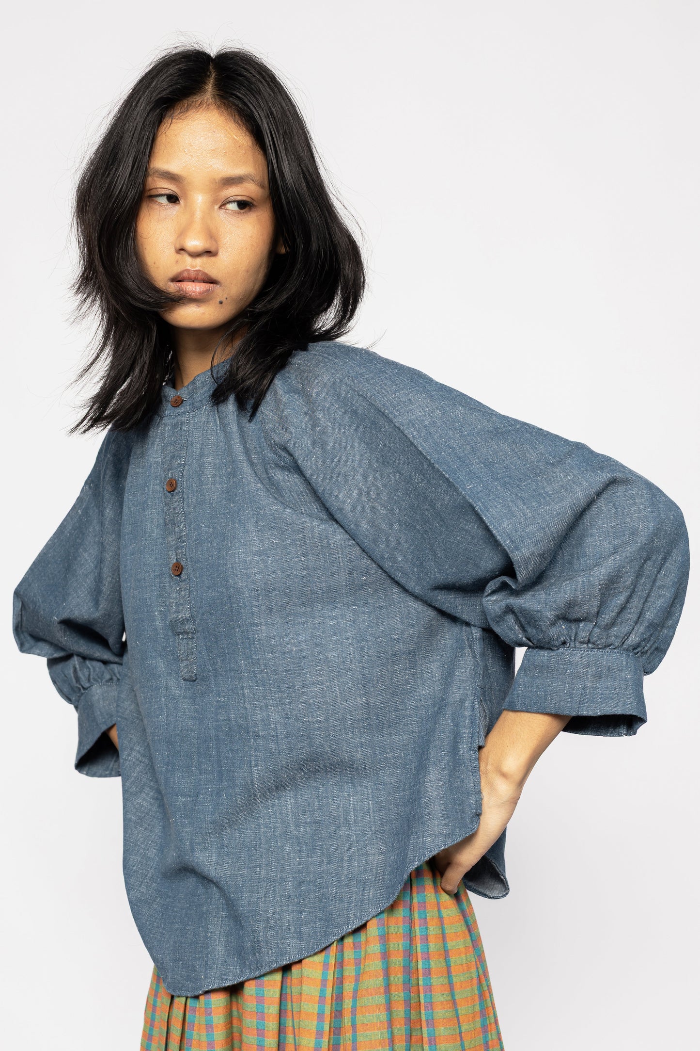 Plains Design - Sault wide sleeved top. Closeup of blue denim wide sleeved top with wooden buttons and side slits in a relaxed fit. Paired with an orange skirt. Ethically handmade in India with handspun cotton twill denim.