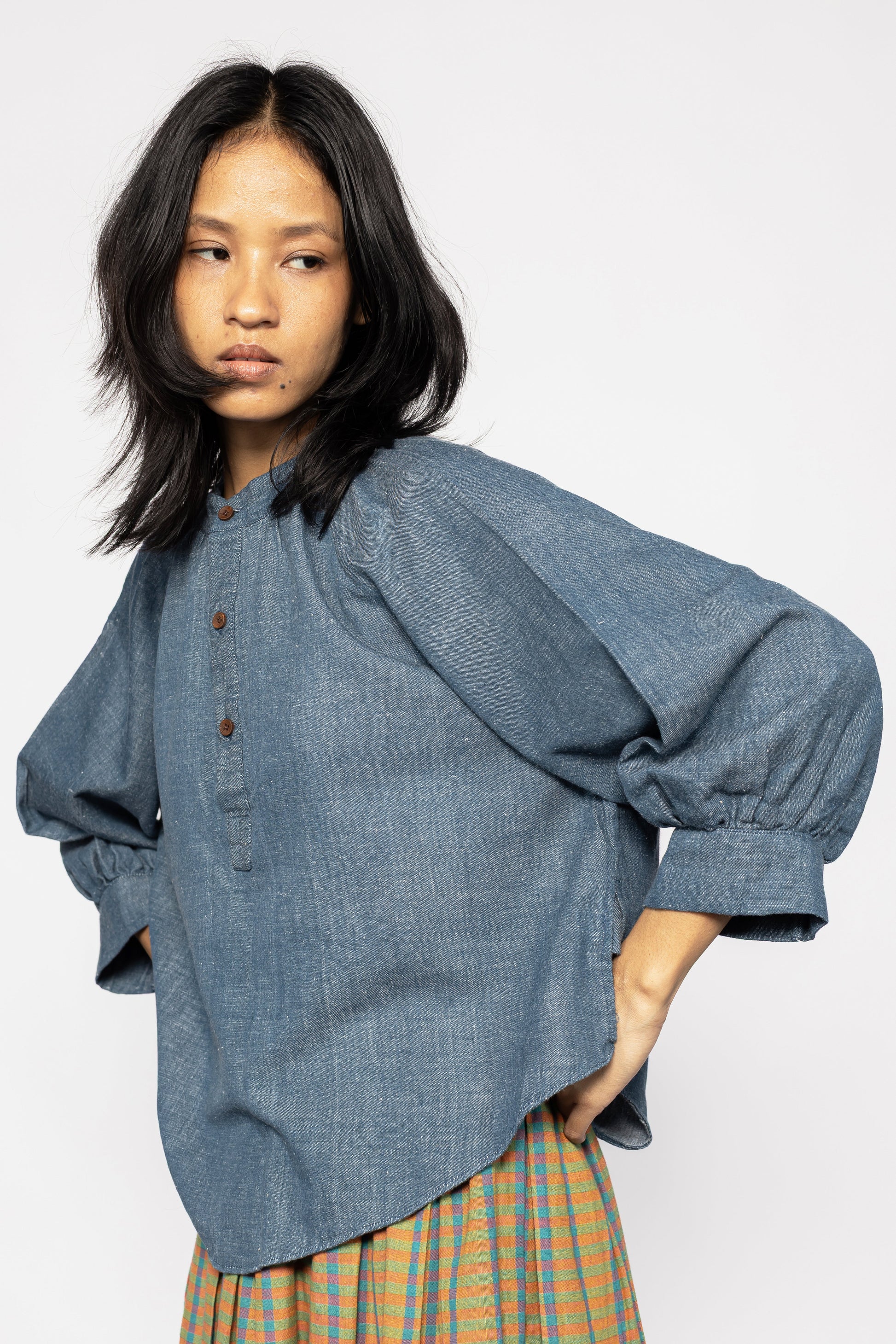 Plains Design - Sault wide sleeved top. Closeup of blue denim wide sleeved top with wooden buttons and side slits in a relaxed fit. Paired with an orange skirt. Ethically handmade in India with handspun cotton twill denim.
