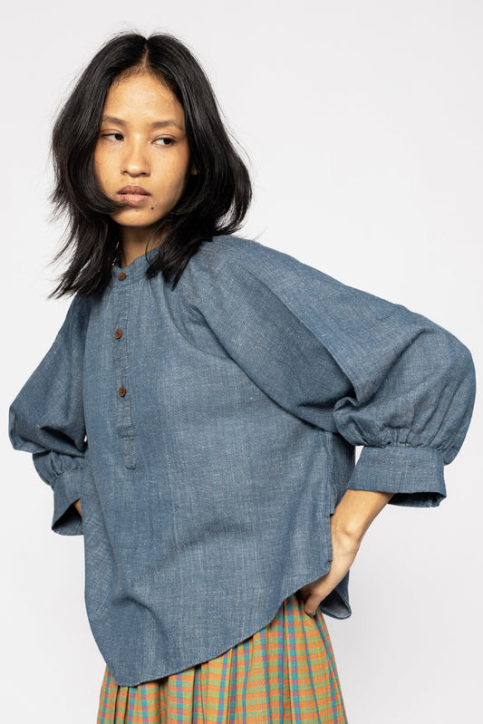Plains Design - Sault wide sleeved top. Closeup of blue denim wide sleeved top with wooden buttons and side slits in a relaxed fit. Paired with an orange skirt. Ethically handmade in India with handspun cotton twill denim.