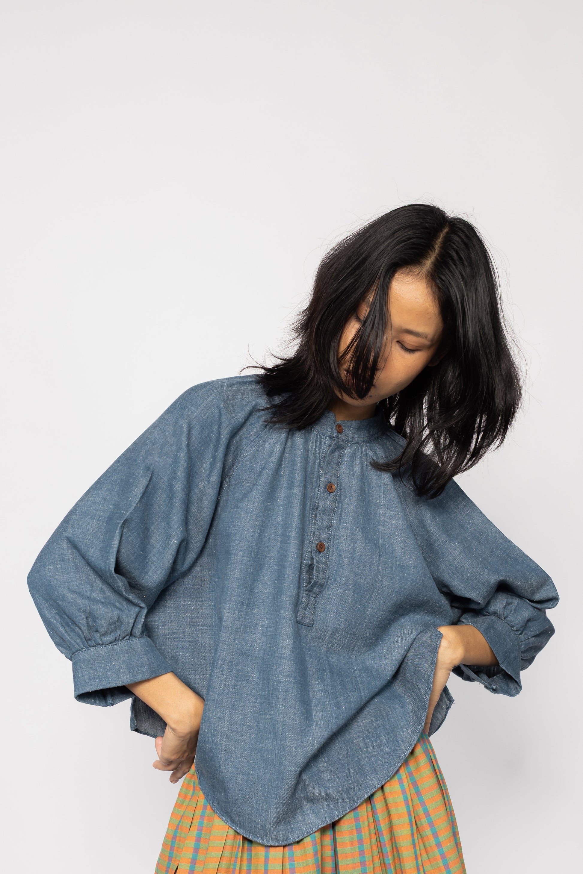 Plains Design - Sault wide sleeved top. Closeup of blue denim wide sleeved top with wooden buttons and side slits in a relaxed fit. Paired with an orange skirt. Ethically handmade in India with handspun cotton twill denim.
