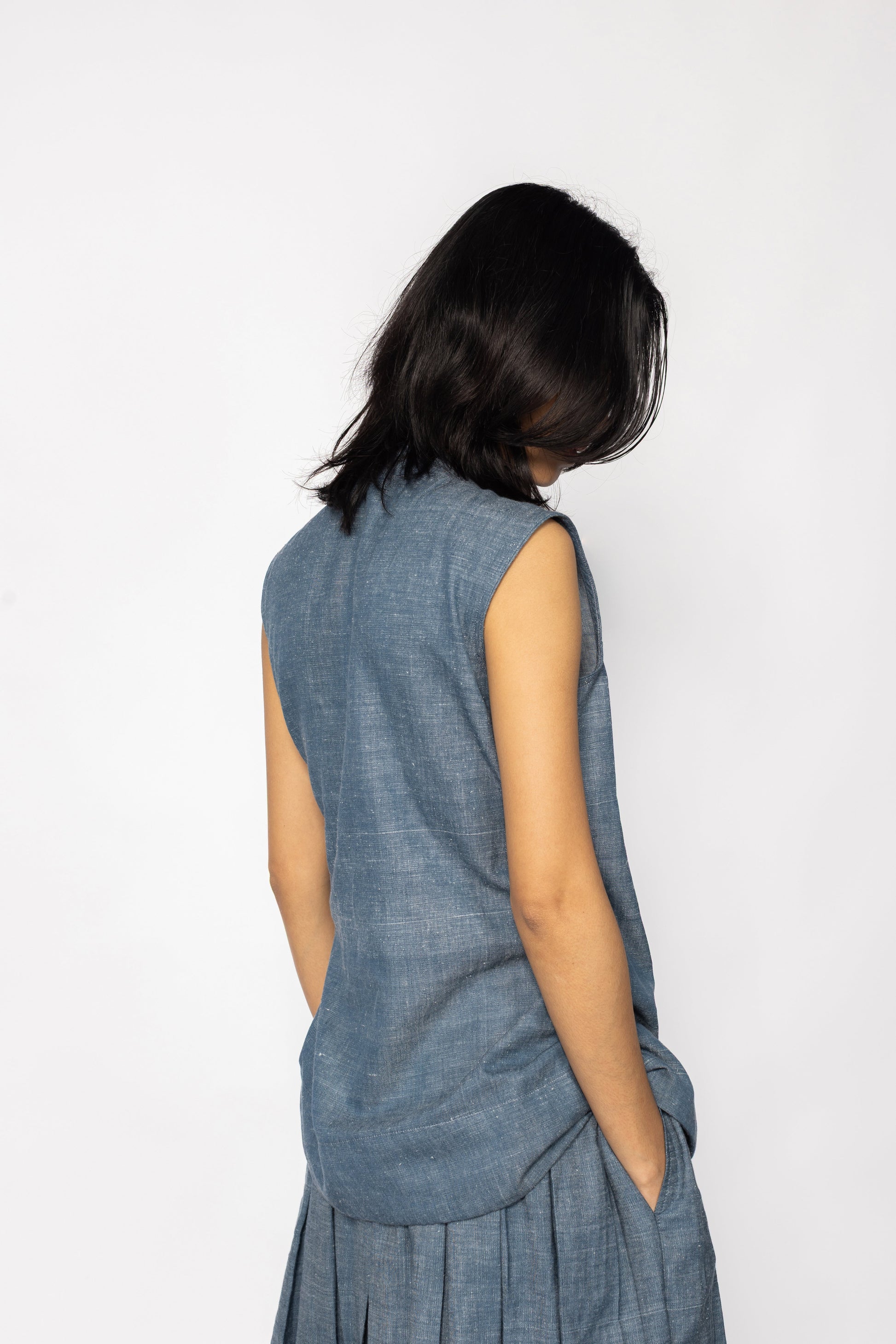 Plains Design - Wave Denim Wrap Top. Back view of blue denim sleeveless wrap top, paired with a skirt of the same fabric. The denim is ethically handmade in cotton twill.