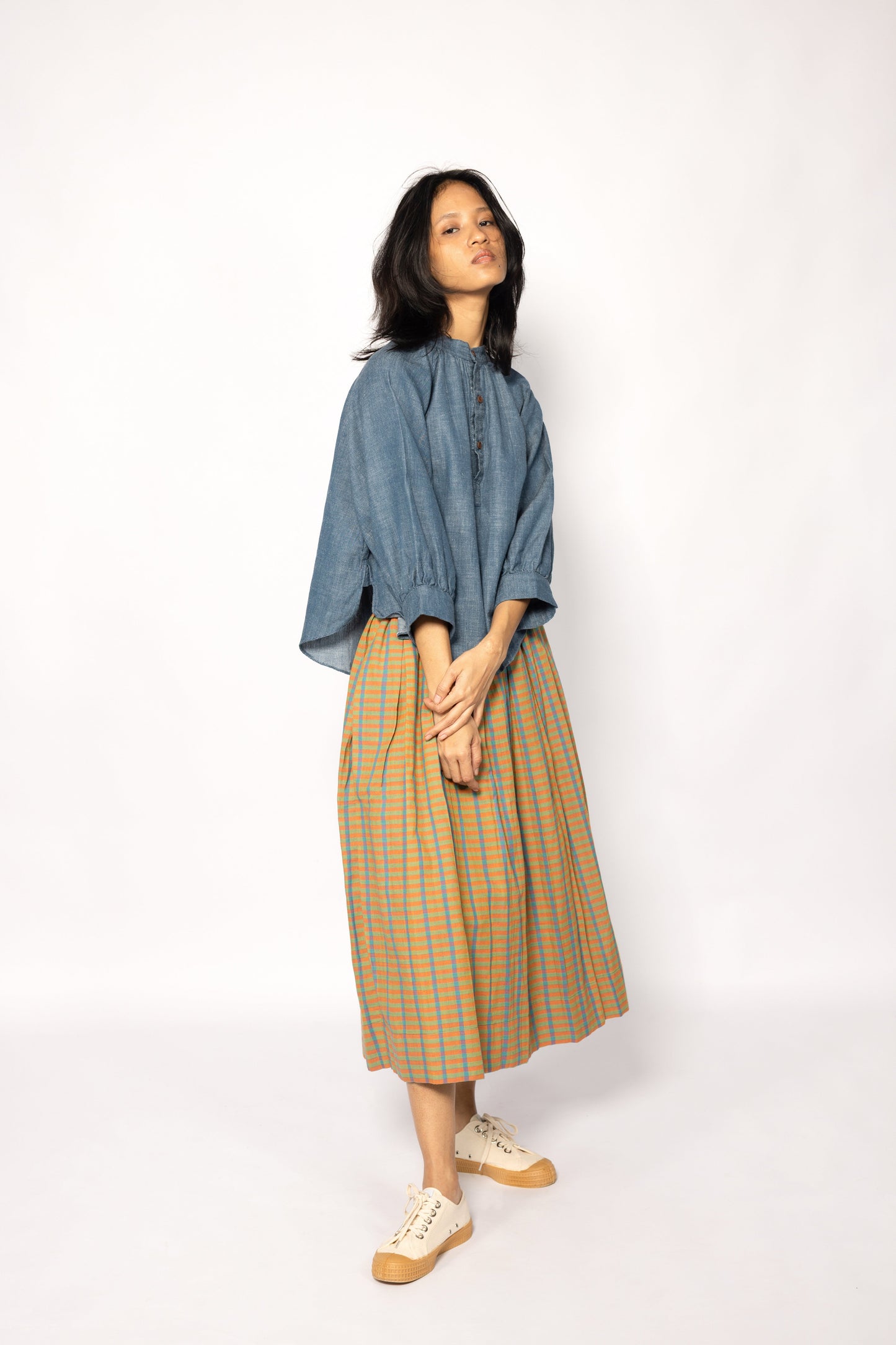 Plains Design - Twin skirt in Orange. Midi skirt with orange, blue and yellow checks in a relaxed fit and side pockets. Paired with a denim top and canvas shoes. Ethically handmade with handspun cotton in India.