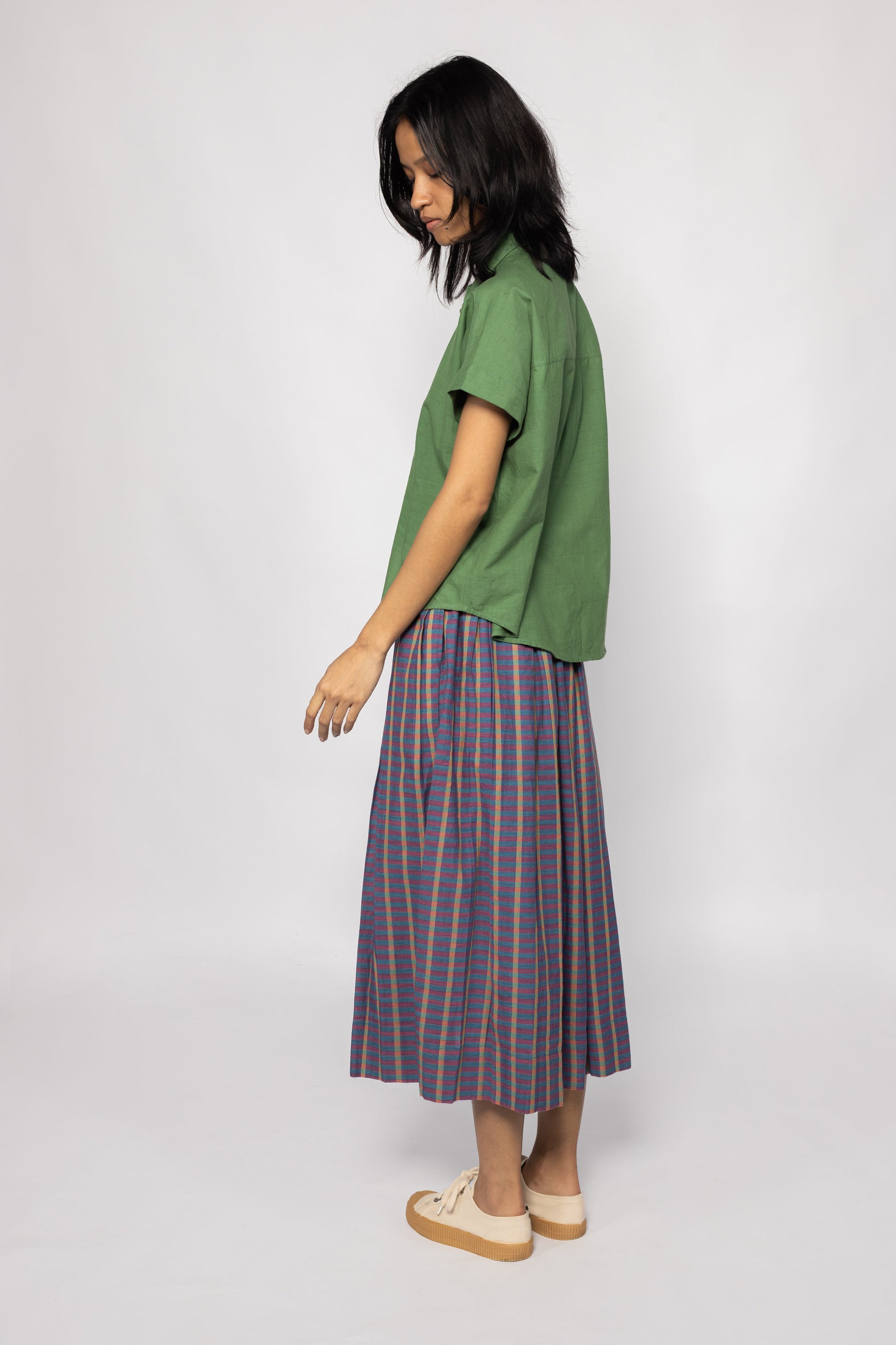 Plains Design - Twin Skirt in Purple. Side of view woman wearing purple striped skirt with pockets paired with a green shirt and canvas shoes. Handmade cotton. Ethical fashion.