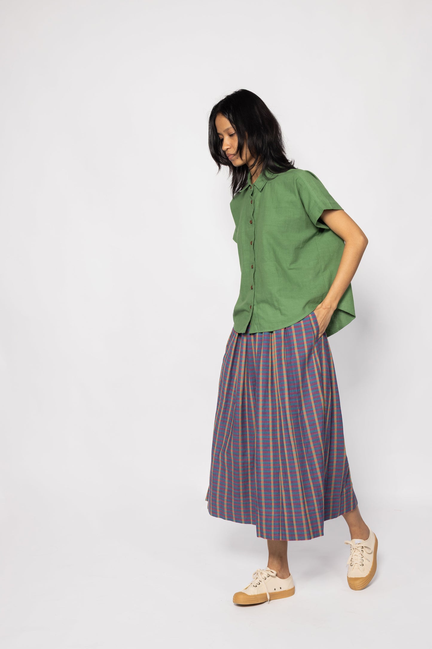 Plains Design - Twin Skirt in Purple. Woman walking in purple and blue striped skirt with pockets, paired with a green shirt and canvas shoes. Handmade cotton. Ethical fashion.